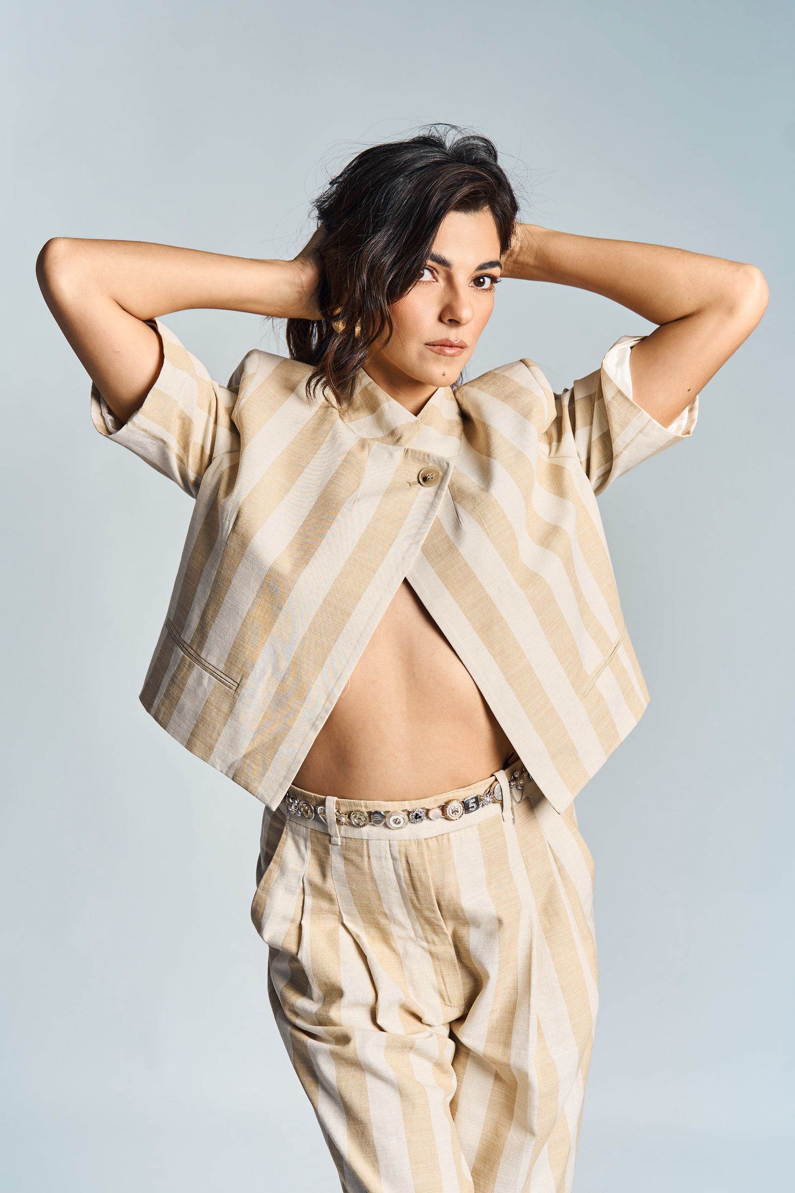Striped cropped jacket and trousers, hands behind the head, pale blue ground.