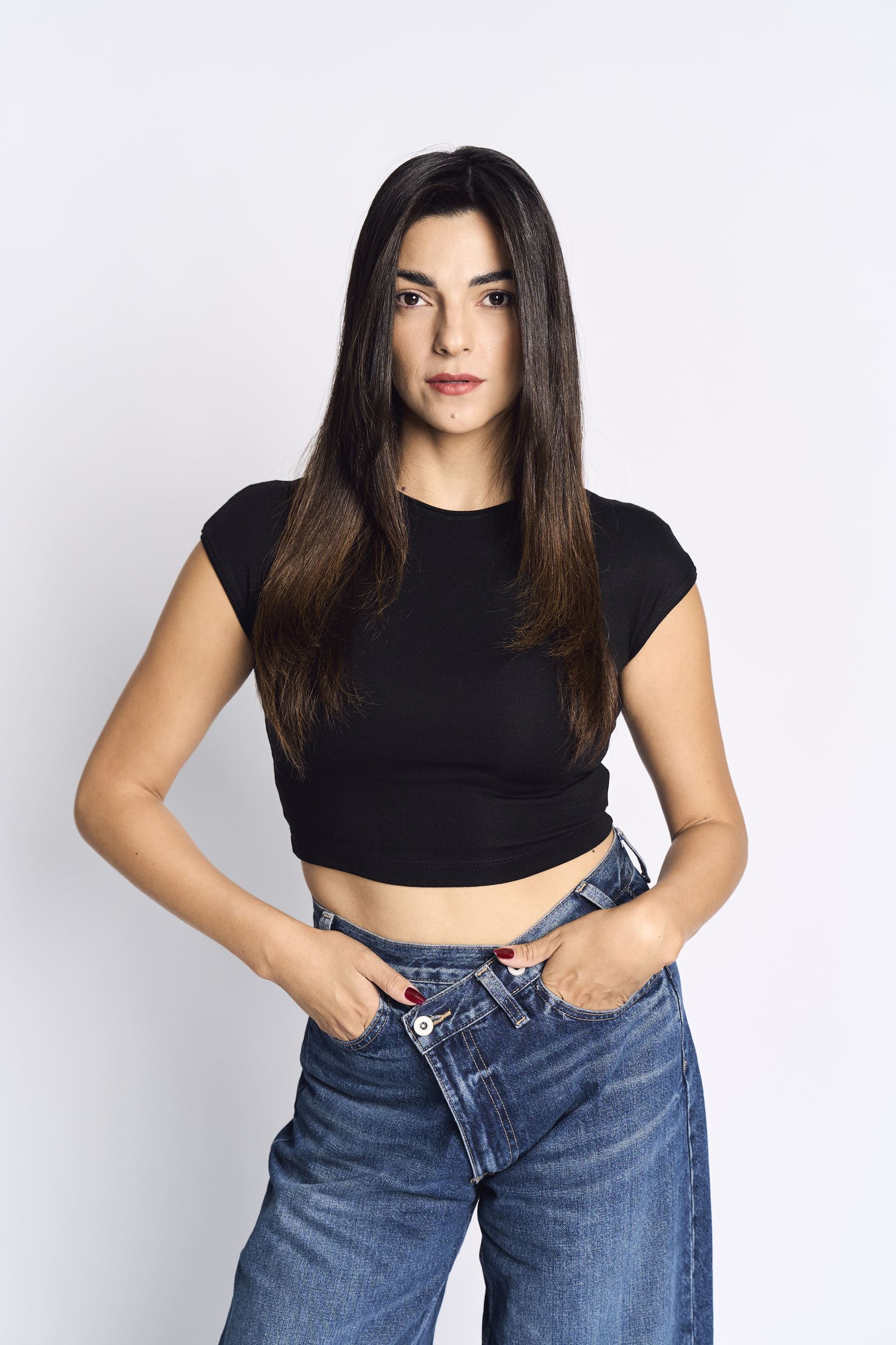 Black crop top and jeans, thumbs hooked into the pockets, even studio light.