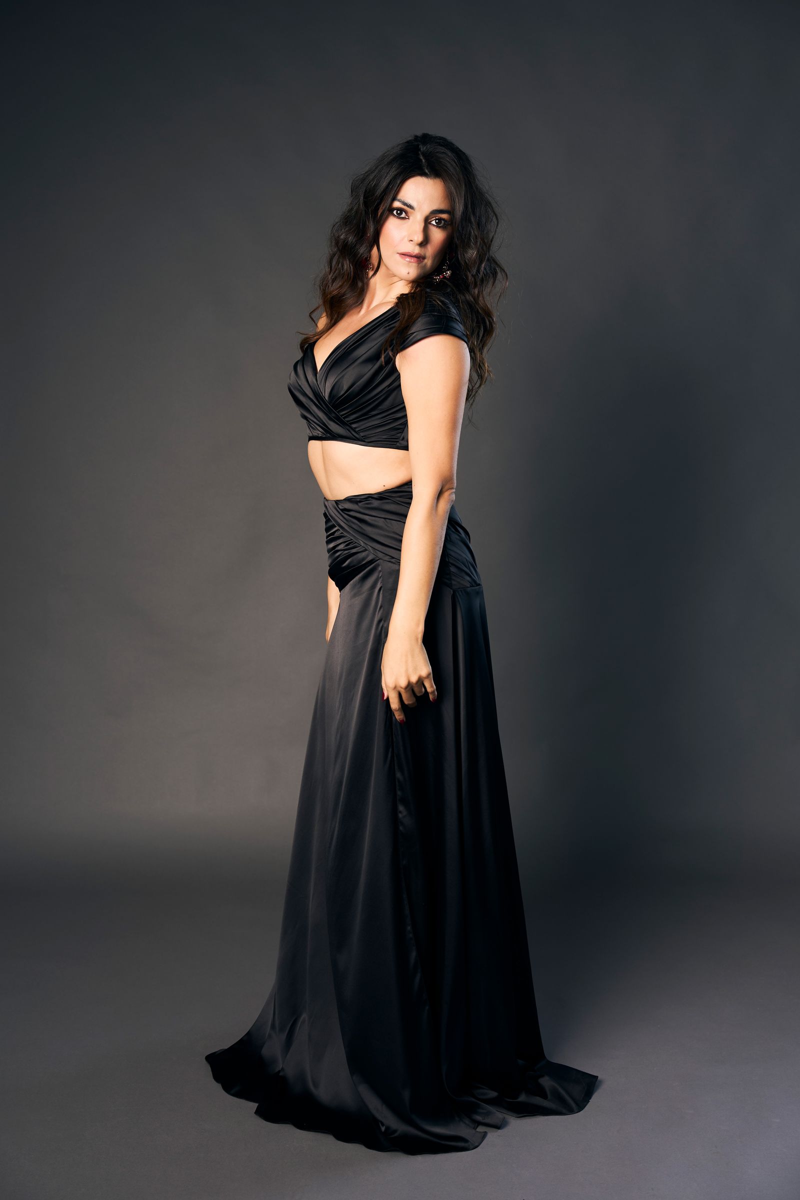 Black satin gown, a look back over the shoulder in three-quarter pose under soft studio light.