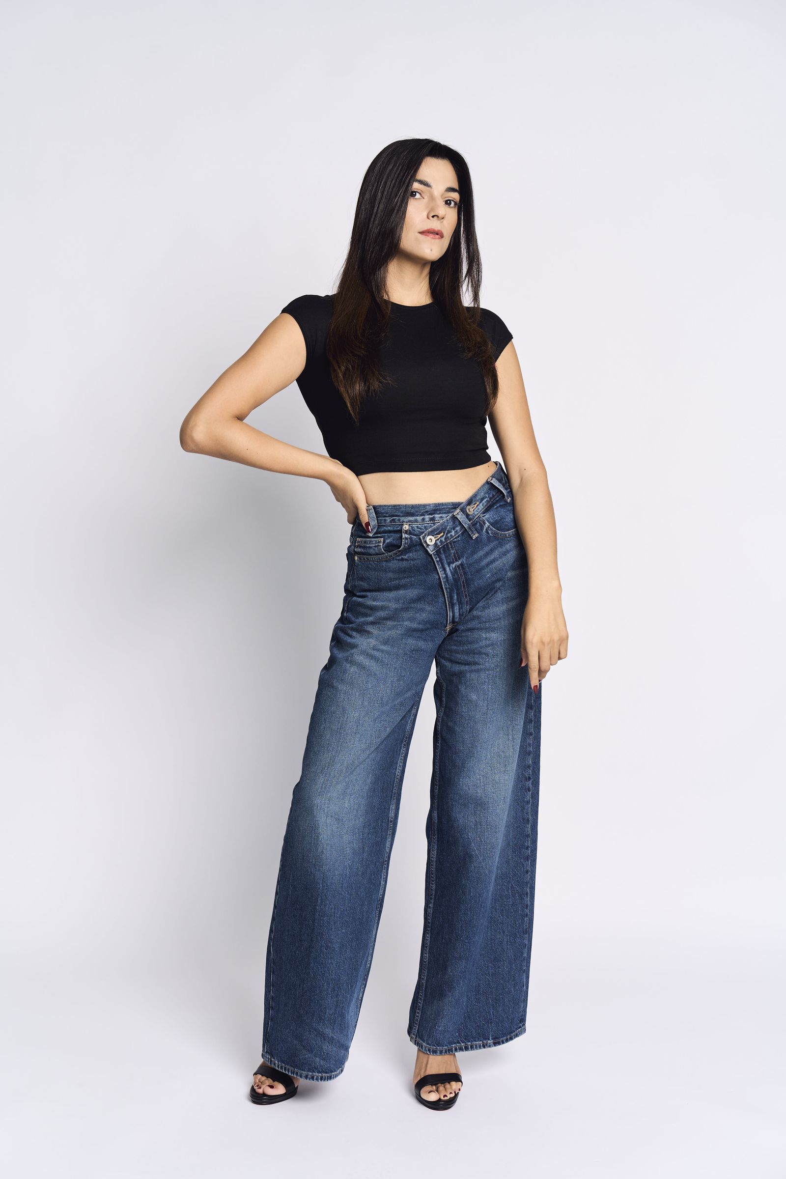 Black top and wide-leg jeans, hip pushed out, brightly lit studio.